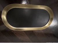 Top view of an oval bar tray with gold stainless steel frame and black leather inset, showing full shape and dimensions.