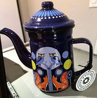 Front view of the dark blue enamel coffee pot showing the folklore design with owls, tree, foxes, and circular motifs.