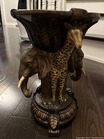 Side view showing two elephants and a giraffe forming the support of the wooden plant stand with decorative base and round top tray.