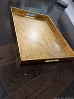 Golden-yellow lacquered rectangular serving tray with cutout handles viewed from an angle to show depth and marbled pattern on tray surface.