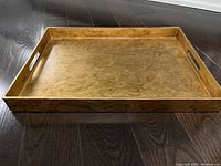 Top-down angled photo showing wood grain lacquer surface and raised edges with cutout handles.