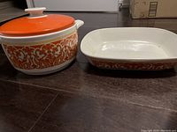 Two Royal Doulton fine oven china dishes on floor: round casserole with orange lid and matching rectangular dish with white interior and orange decorative border.
