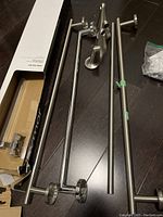 Several metal towel bars including single and double bars with mounting brackets and some mounting screws and hardware on dark floor.