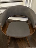 Front view of the upholstered arm chair showing seat and curved backrest upholstery, wooden frame, and legs.