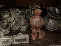 Full set of vintage glassware arranged including clear and painted glass decanter, shot glasses, water jugs, espresso cups, and butter dishes