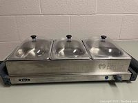 Front view of the triple buffet server with three clear lids over chafing dishes on stainless steel base