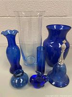 The lot of seven blue glass items arranged together showing variety of shapes and shades of blue glass.