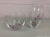 Full view of the crystal bowl and vase with purple floral designs placed side by side against a wall.