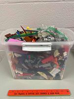 Clear plastic tote filled with assorted building blocks and mini-figure pieces, viewed from front and above angles.