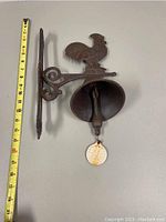 Cast iron rooster bell with measuring tape alongside showing approx 9 inches in height.