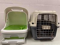 Plastic litter box and cat carrier shown side by side, litter box is white with green interior and includes a scoop; cat carrier is beige and gray with metal wire door.
