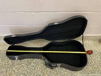 Open black hard shell guitar case with tape measure showing length inside around 41.5 inches.