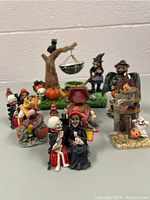 Full view of the lot showing seven assorted Halloween-themed knickknacks grouped together on a flat surface. Includes witches, skeletons, pumpkins, and small spooky scenes.