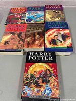 Full set of 7 Harry Potter books with illustrated covers. Displayed with 3 books in front and 4 behind. Covers show series title and author J.K. Rowling.