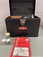 Closed black metal carrying case with Craftsman decal. Power router handle visible inside the open case, plus an instruction manual and three small plastic containers with router bits on top of the case.