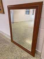 Full view of the large rectangular mirror showing the wooden frame and clear glass surface reflecting a hallway and wall.