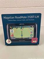 Front of the box showing Magellan RoadMate 2120T-LM GPS with display and key advertised features like lifetime maps and traffic.