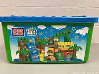 Green and blue plastic Mega Bloks First Builders branded storage tote showing graphic of jungle-themed block animals and characters on the front.