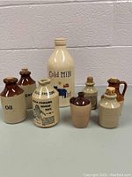 Full view of 8 mini vintage ceramic jugs and bottles on display showing different labels and colors.