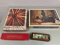 Photo showing all four items: two sealed jigsaw puzzles and two boxed domino sets.