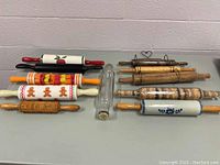Full view of 11 wooden rolling pins and one vintage Roll-Rite clear glass rolling pin jar on table