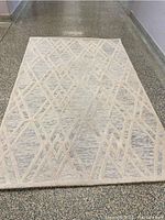 Full view of the Safavieh 5x8 area rug laid on a textured floor showing beige and cream geometric overlapping diamond pattern.