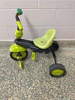 Left side view of Smart Trike child's tricycle with green seat and black frame on a speckled floor, showing overall structure and colors.