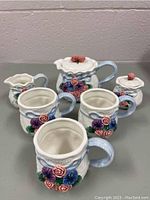 Full set viewed from front, shows 3 mugs, teapot, creamer, sugar dish with floral 3D decoration.