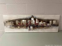 Full view of the rectangular textured painting on canvas against a wall showing an abstract city skyline in neutral and red tones.