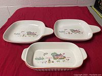 Three vintage ceramic dishes with country house and farm animal prints on a red cloth background.