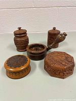 Front view of four carved wooden boxes and one candle holder displayed against a wall.