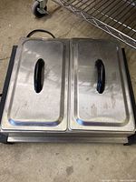 Top view of the Bravetti electric buffet server showing two stainless steel lids with black handles on metal compartments.