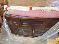 Front view of wood buffet cabinet covered partially in plastic with fabric rolls on top