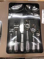 Initial view of some cutlery pieces in black tray showing hammered finish handles, includes various forks, knives, and spoons.