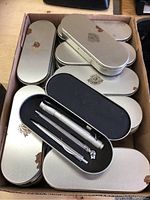 Box with 23 silver metal oval cases stacked, showing rust spots on cases.