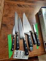 Six kitchen knives arranged side by side on wood surface labeled with tag noting Cuisinart and Henckels cutters.