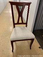 Front view of a side dining chair showing cherrywood frame, carved backrest, and light upholstered seat.
