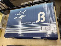 Closed blue box with white text 'Corredo di sogno' and 'S B' branding, containing Italian table linens.