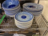 Stacks of 10 deep blue and white floral patterned bowls, 9 dessert plates, and 10 dinner plates with similar design on metal shelving.