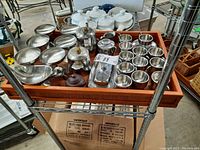 Tray holding multiple small metal cups, a coffee pot, sugar bowl, gravy boat, and butter dish in metal and wood/wicker.