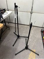 Two black microphone stands side by side on a concrete floor. One stand has an adjustable boom arm and a spacious tripod base, identified as the Yorkville MS657B.