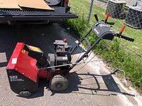 Side view of red Noma 523 snow blower showing large front auger, wheels, and control handles.