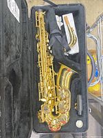 Opened hard case showing alto saxophone body, neck, and accessories in compartments