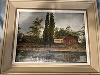 Overview of the antique mid-century oil painting with landscape view of buildings and trees by water.