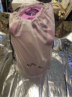 Light pink drawstring fabric cover containing the water bottle, standing upright on reflective surface.
