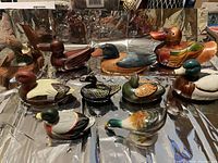 Ten decorative duck figurines arranged on a reflective surface, displaying various realistic and stylized designs.