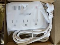 New white multifunctional power strip with USB ports partially wrapped in plastic inside its box.