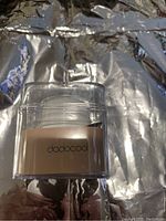Dodocool branded gold mini wireless speaker in clear plastic packaging, showing front with brand name.