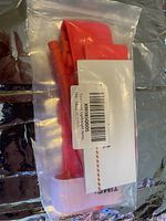 Front view of the tourniquet in clear plastic packaging showing the red strap and plastic windlass rod.