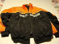 Front view of extra large Harley Davidson jacket showing black and orange color scheme with embroidered Harley Davidson text and logos.